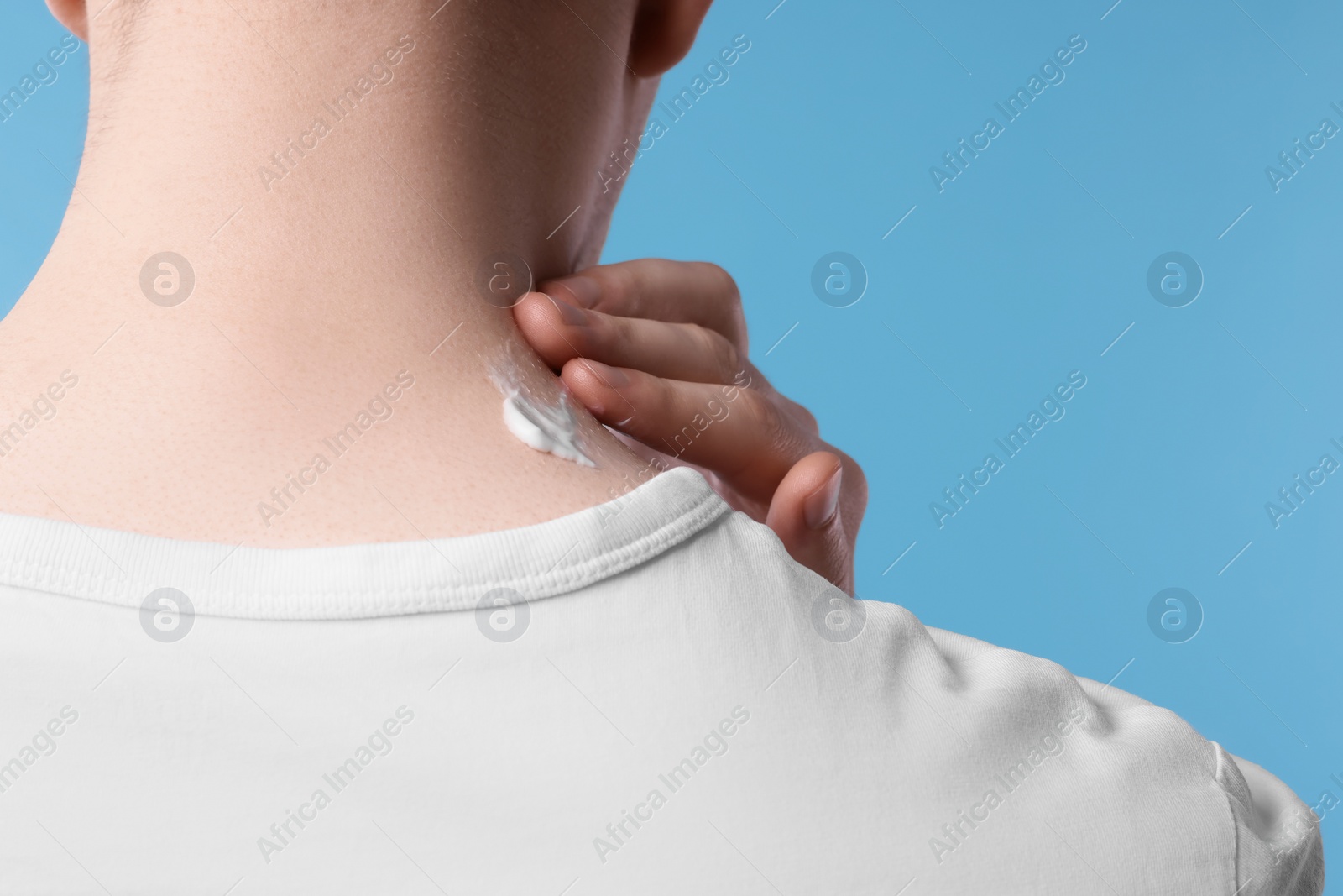 Photo of Man applying ointment onto his neck on light blue background, closeup
