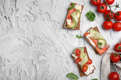 Photo of Tasty rye crispbreads with salmon, cream cheese and vegetables on grey textured table, flat lay. Space for text