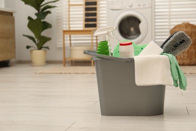 Different cleaning products in bucket on floor indoors, space for text