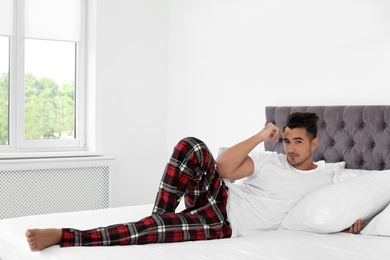 Photo of Young man lying on bed with soft pillows at home
