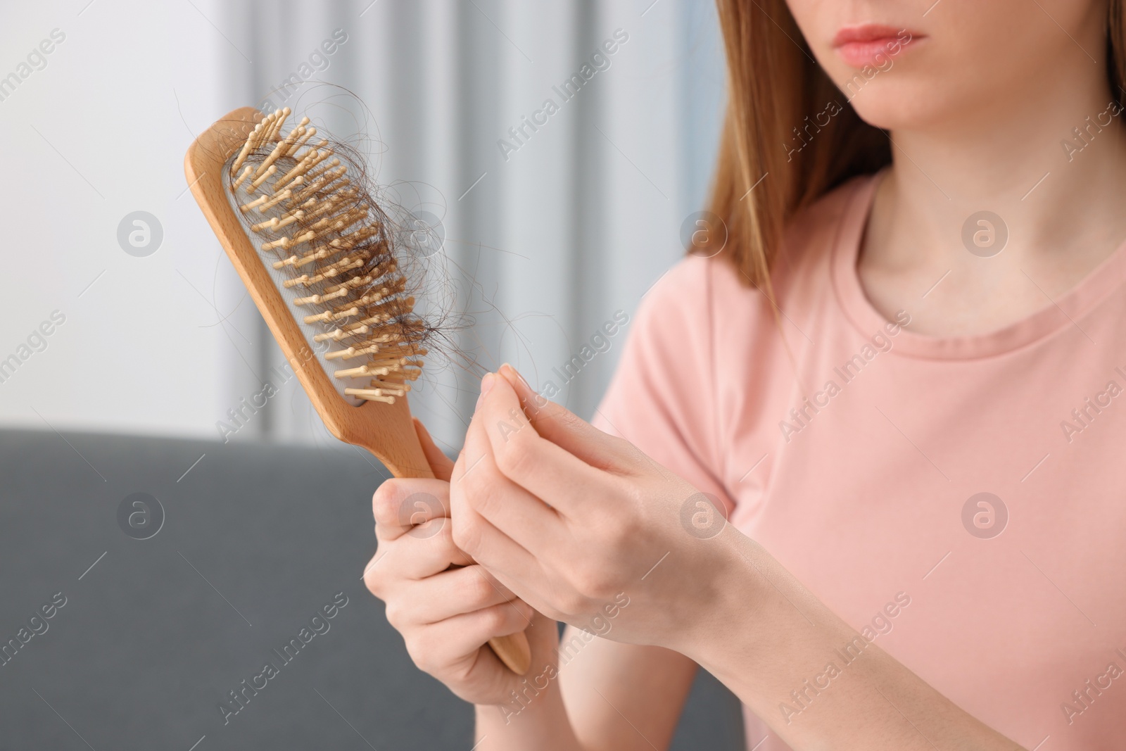 Photo of Woman untangling her lost hair from brush indoors, closeup. Alopecia problem