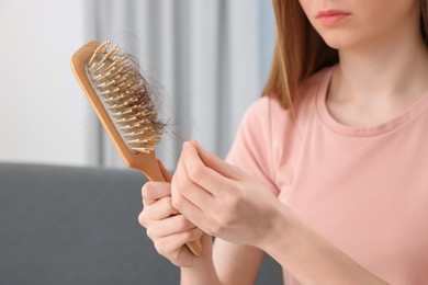 Woman untangling her lost hair from brush indoors, closeup. Alopecia problem