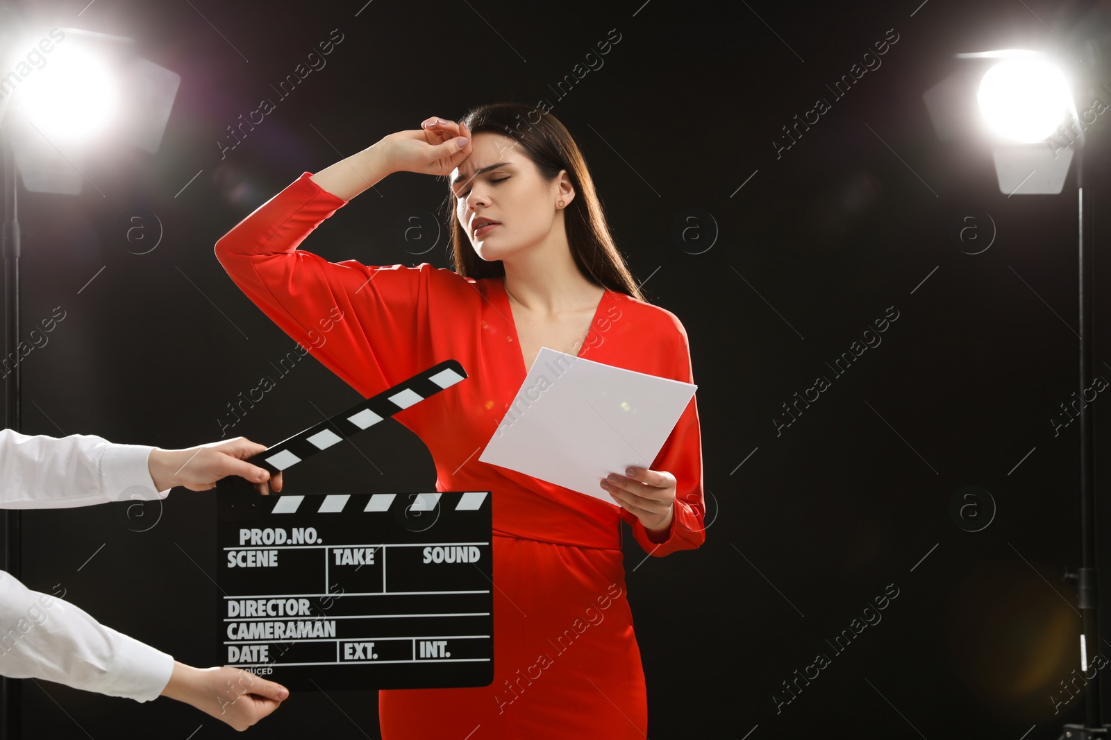 Photo of Emotional actress performing role while second assistant camera holding clapperboard on stage. Film industry