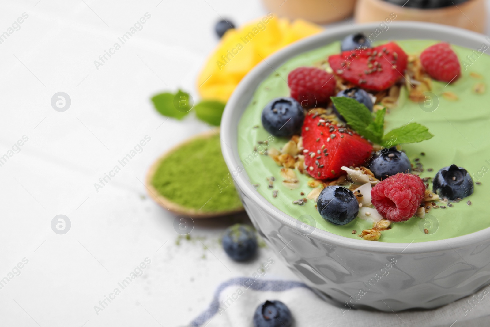 Photo of Tasty matcha smoothie bowl served with berries and oatmeal on white table, closeup with space for text. Healthy breakfast