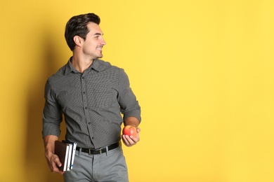 Young male teacher with books and apple on yellow background. Space for text