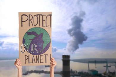 Image of Protestor holding placard with text Protect Our Planet and blurred view of industrial factory on background. Climate strike