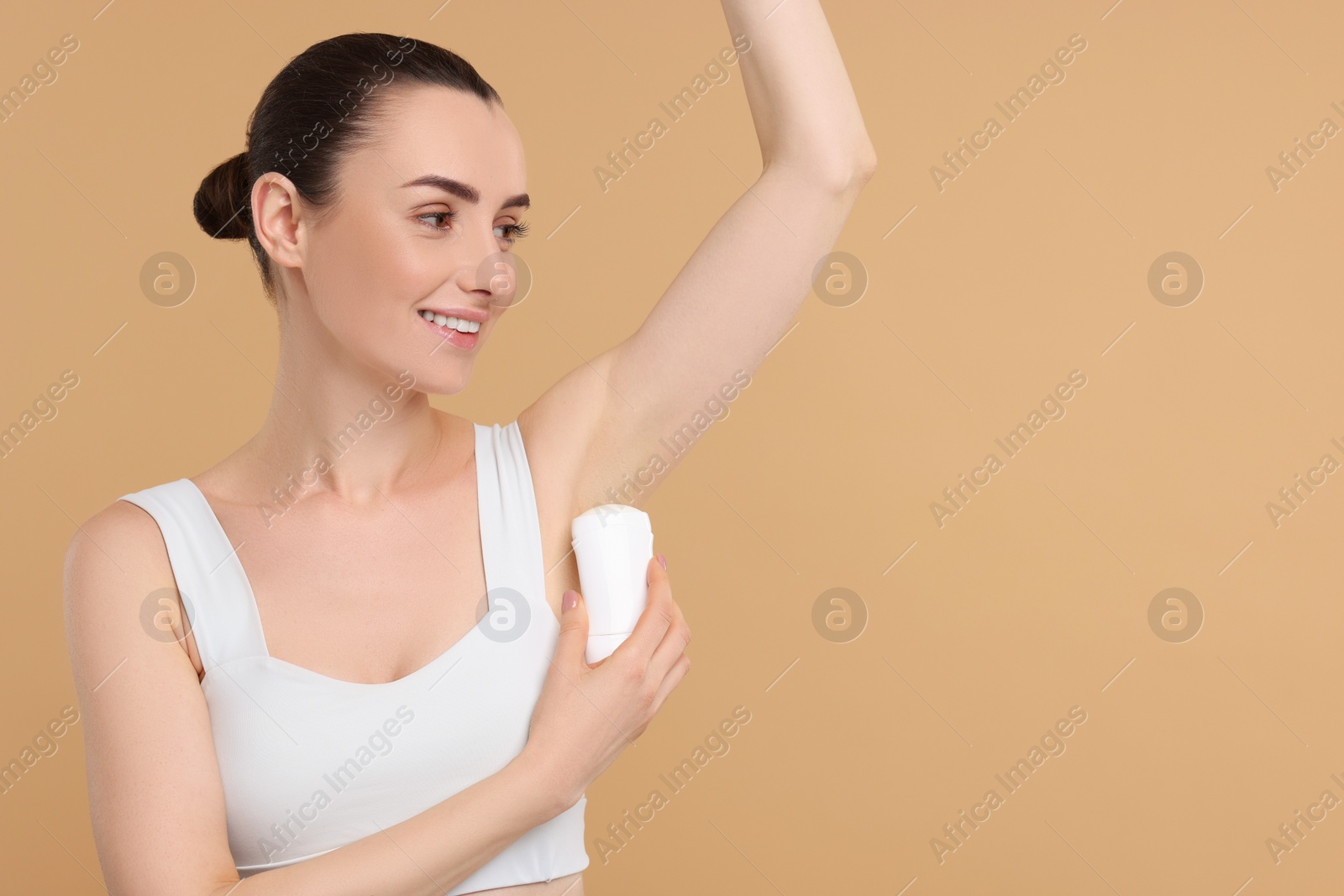 Photo of Beautiful woman applying deodorant on beige background, space for text