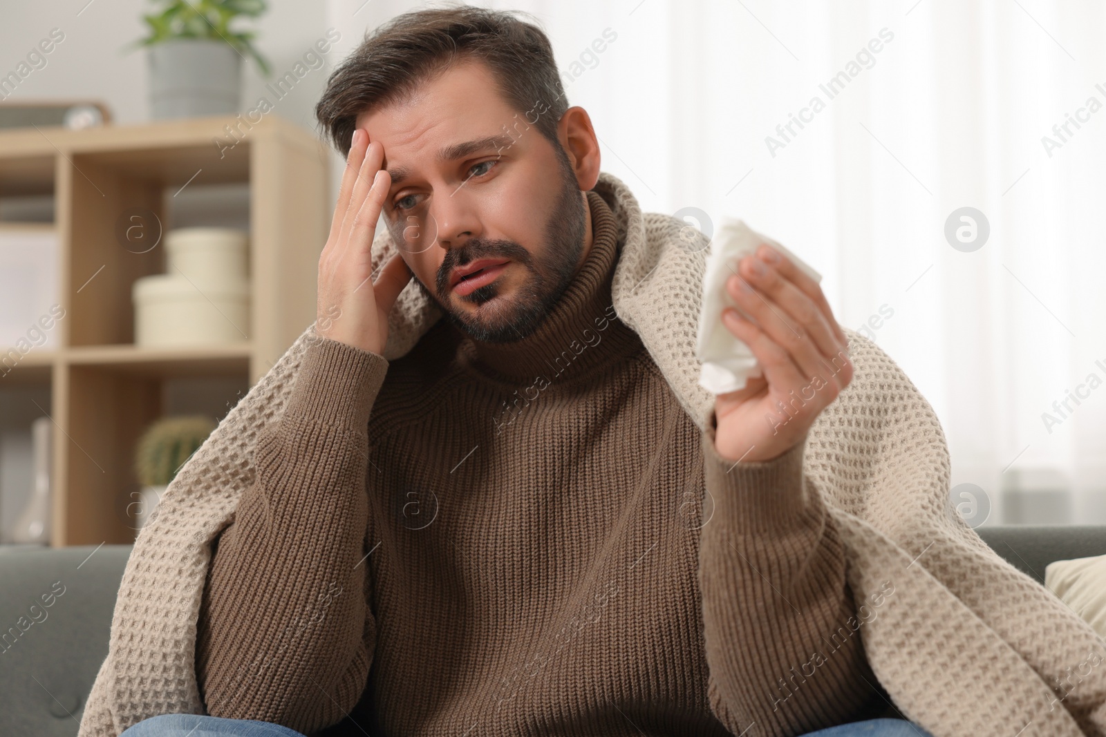 Photo of Sick man with tissue wrapped in blanket on sofa at home. Cold symptoms