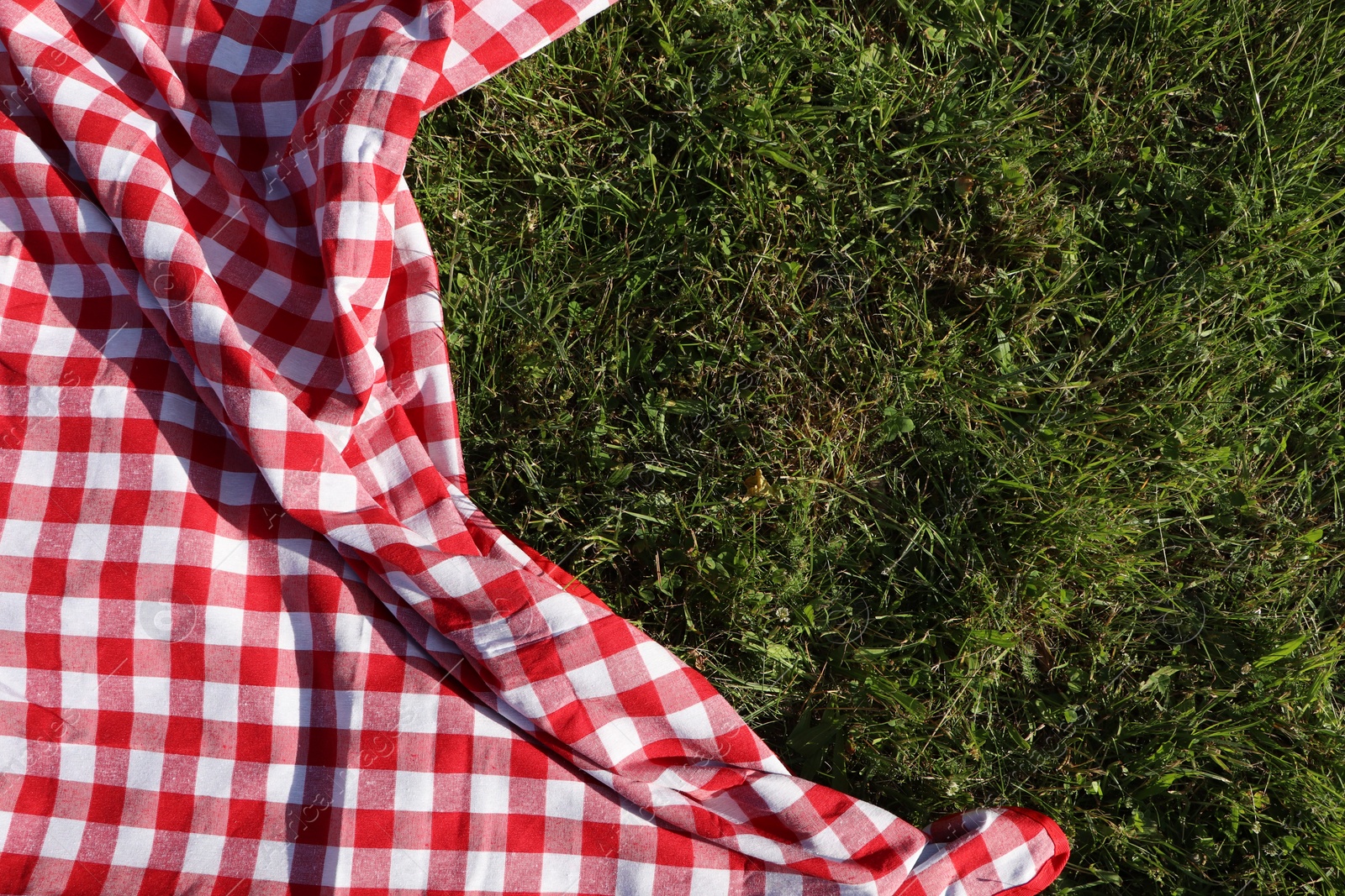 Photo of Checkered picnic tablecloth on fresh green grass, top view. Space for text