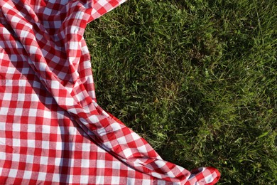 Checkered picnic tablecloth on fresh green grass, top view. Space for text