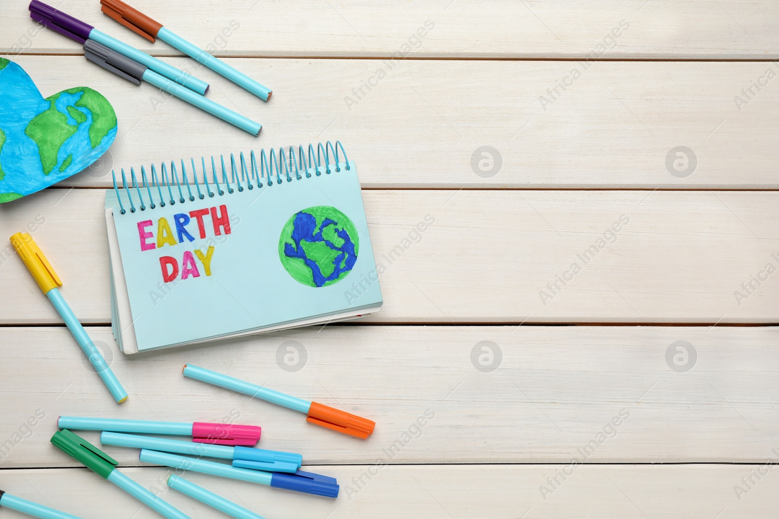 Photo of Happy Earth Day. Flat lay composition with notebook and markers on white wooden table, space for text