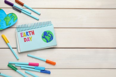 Photo of Happy Earth Day. Flat lay composition with notebook and markers on white wooden table, space for text
