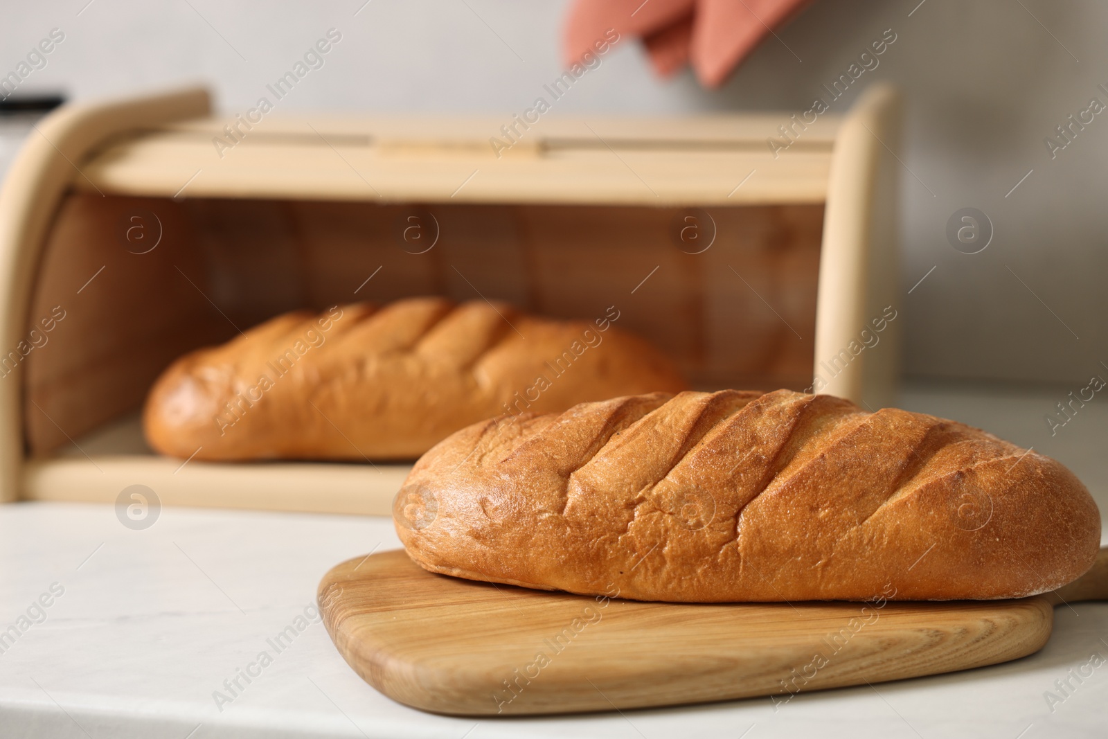 Photo of Wooden bread basket with freshly baked loaves on white marble table in kitchen