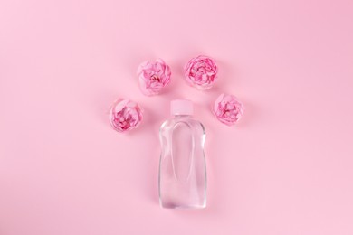 Photo of Bottle with baby oil and beautiful flowers on pink background, flat lay. Space for text