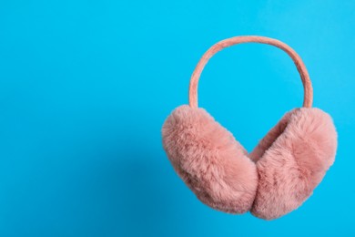 Stylish winter earmuffs on light blue background, space for text