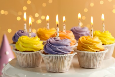 Photo of Tasty birthday cupcakes on white stand against blurred lights, closeup