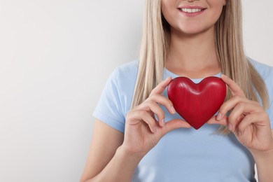 Happy volunteer holding red heart with hands on light background, closeup. Space for text