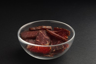 Bowl with pieces of delicious beef jerky on black table