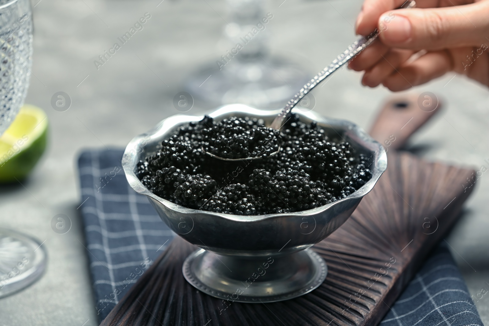 Photo of Woman taking spoonful of black caviar from bowl, closeup