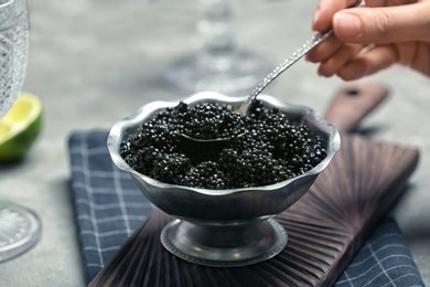 Photo of Woman taking spoonful of black caviar from bowl, closeup