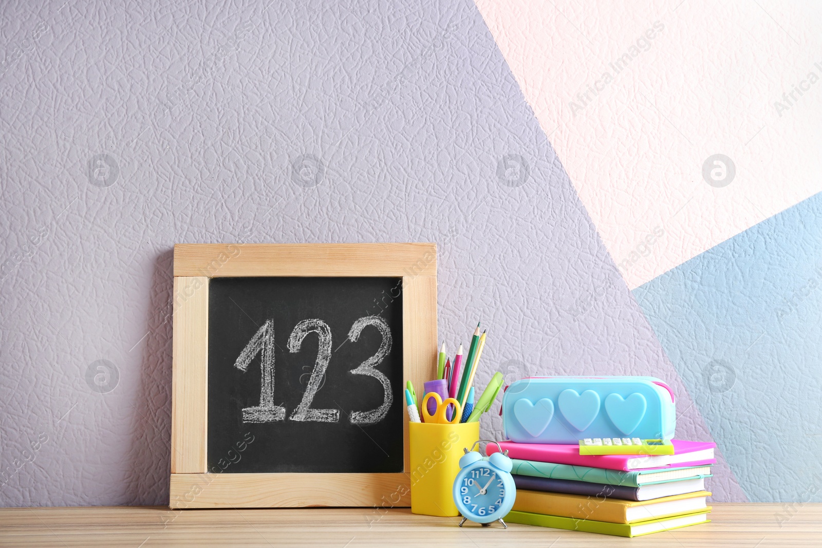 Photo of Different school stationery and small chalkboard on table near color wall