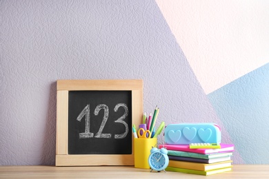 Photo of Different school stationery and small chalkboard on table near color wall