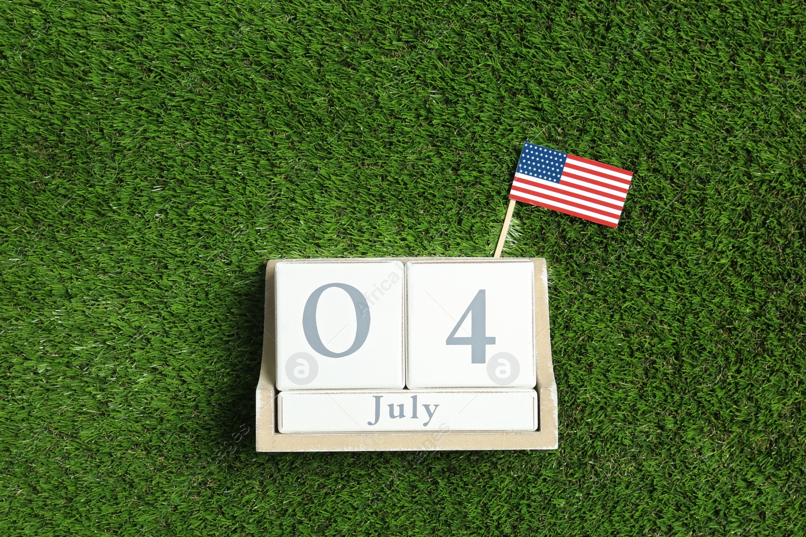 Photo of Wooden calendar with USA flag on green grass, top view. Happy Independence Day