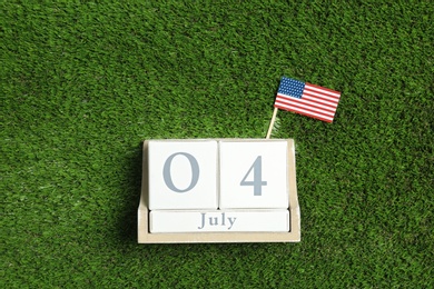 Photo of Wooden calendar with USA flag on green grass, top view. Happy Independence Day