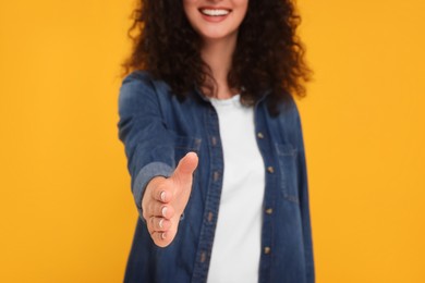 Woman welcoming and offering handshake on yellow background, closeup
