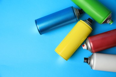 Photo of Cans of different graffiti spray paints on light blue background, flat lay. Space for text