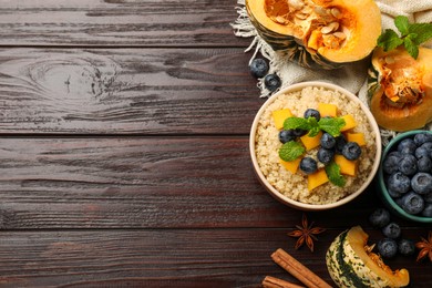 Photo of Flat lay composition with bowl of tasty quinoa porridge, pumpkin and blueberries on wooden table. Space for text