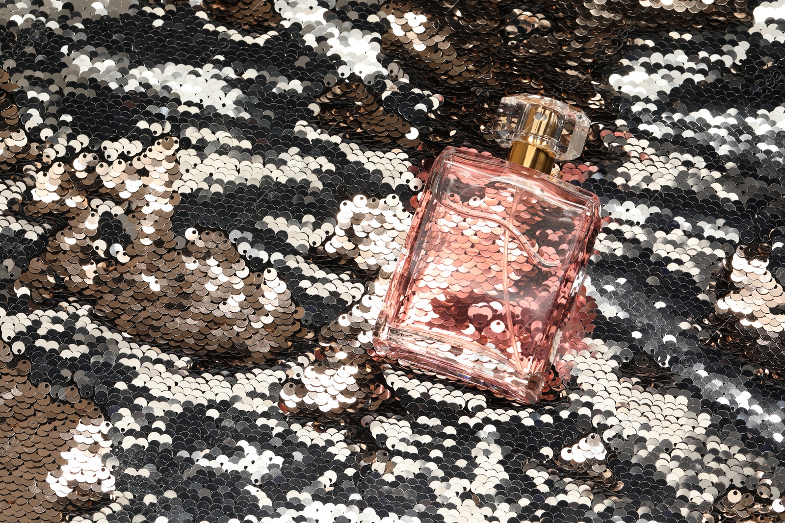 Photo of Luxury perfume in bottle on fabric with silver sequins, top view