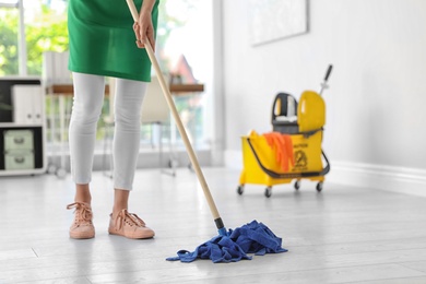 Young woman with mop cleaning floor in office