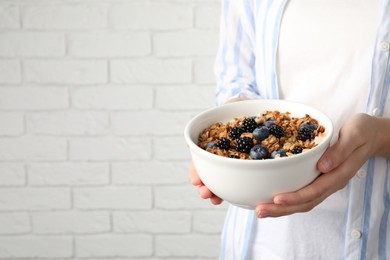 Photo of Woman holding bowl of oatmeal porridge with berries near white brick wall, closeup. Space for text