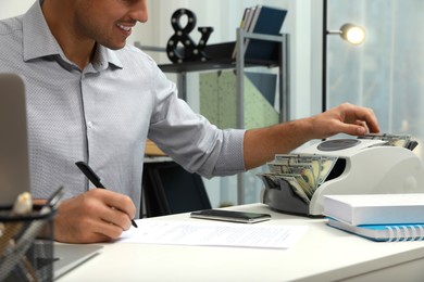 Man using banknote counter at white table indoors, closeup