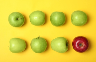 Red apple among green ones on color background, top view. Be different