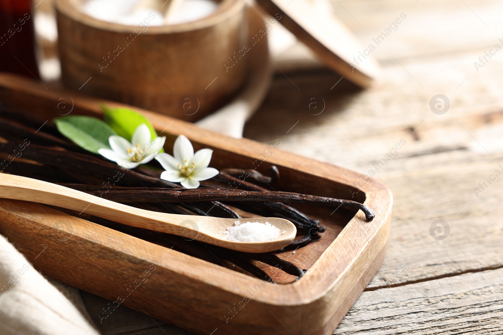 Photo of Vanilla pods, flowers, leaves and spoon with sugar on wooden table, closeup. Space for text