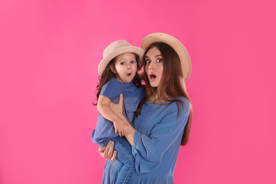 Emotional mother and little daughter with hats on pink background