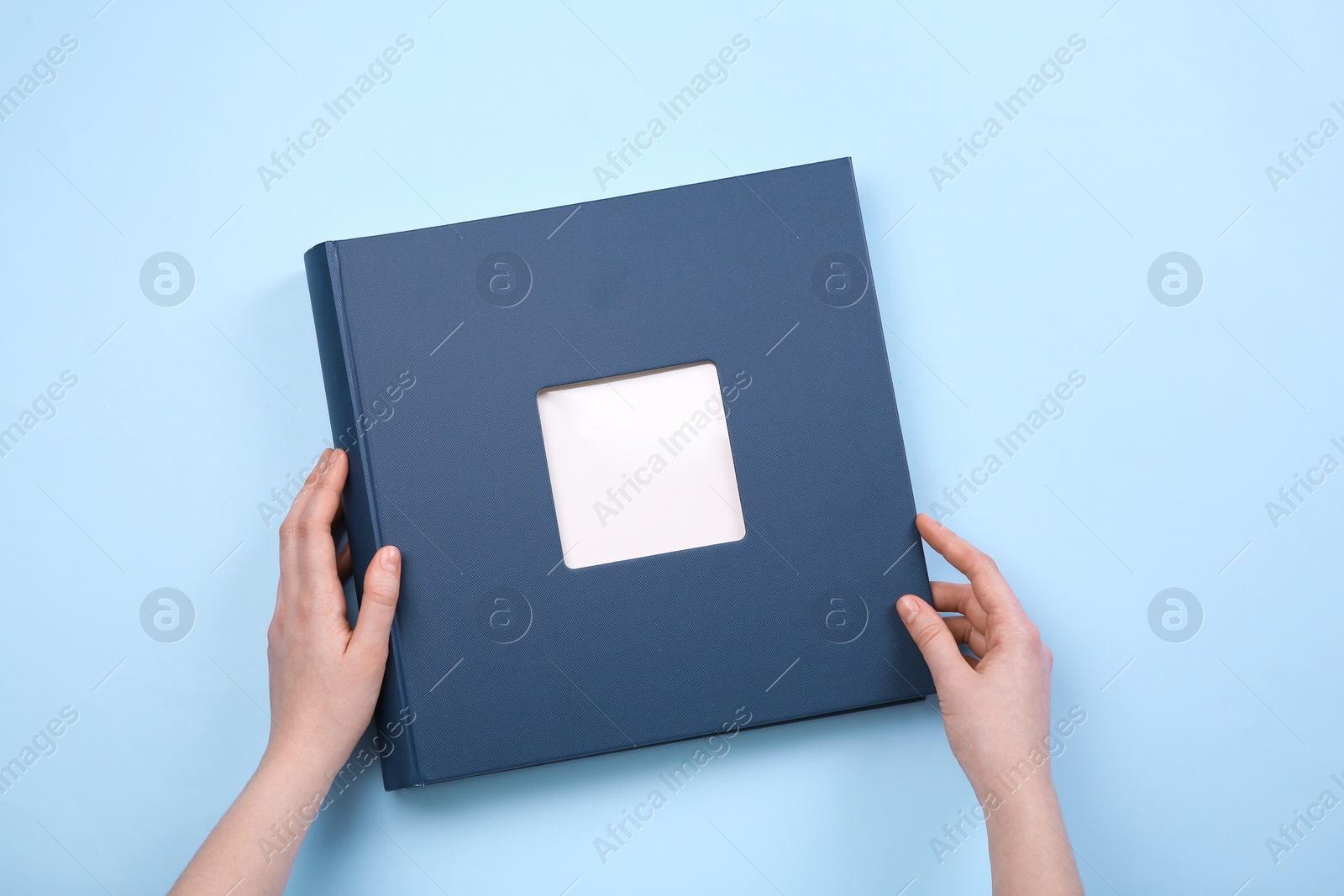 Photo of Woman with photo album at light blue background, top view