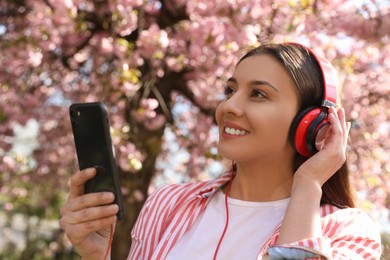 Photo of Young woman with smartphone and headphones listening to music outdoors
