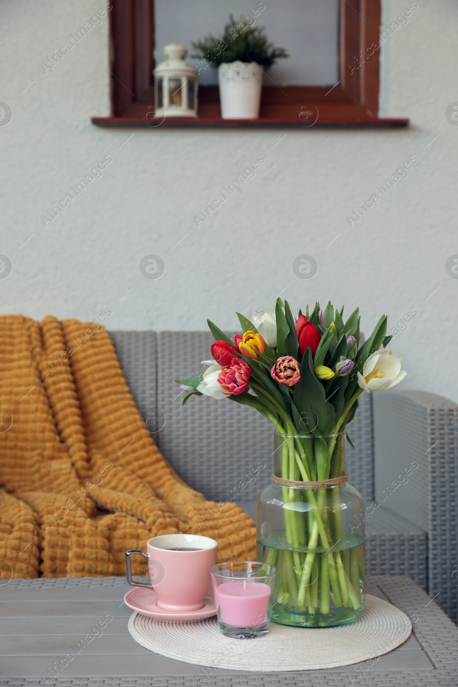 Photo of Beautiful bouquet of colorful tulips, cup with drink and candle on rattan garden table