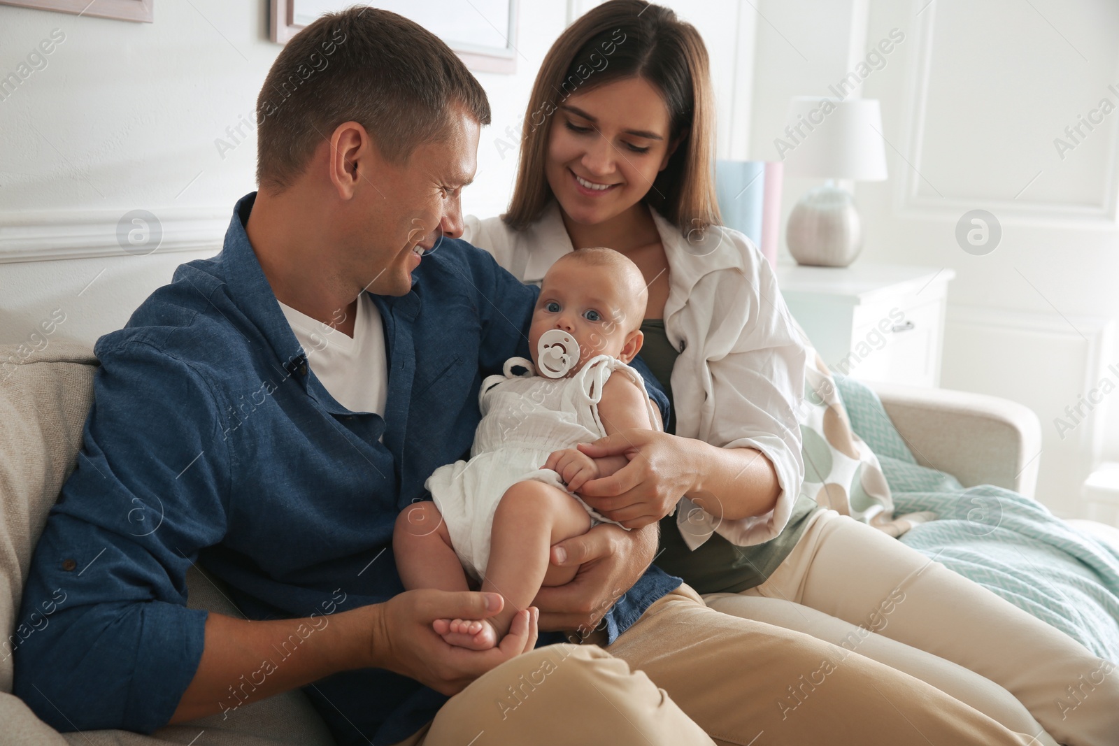 Photo of Happy couple holding their cute little baby with pacifier at home