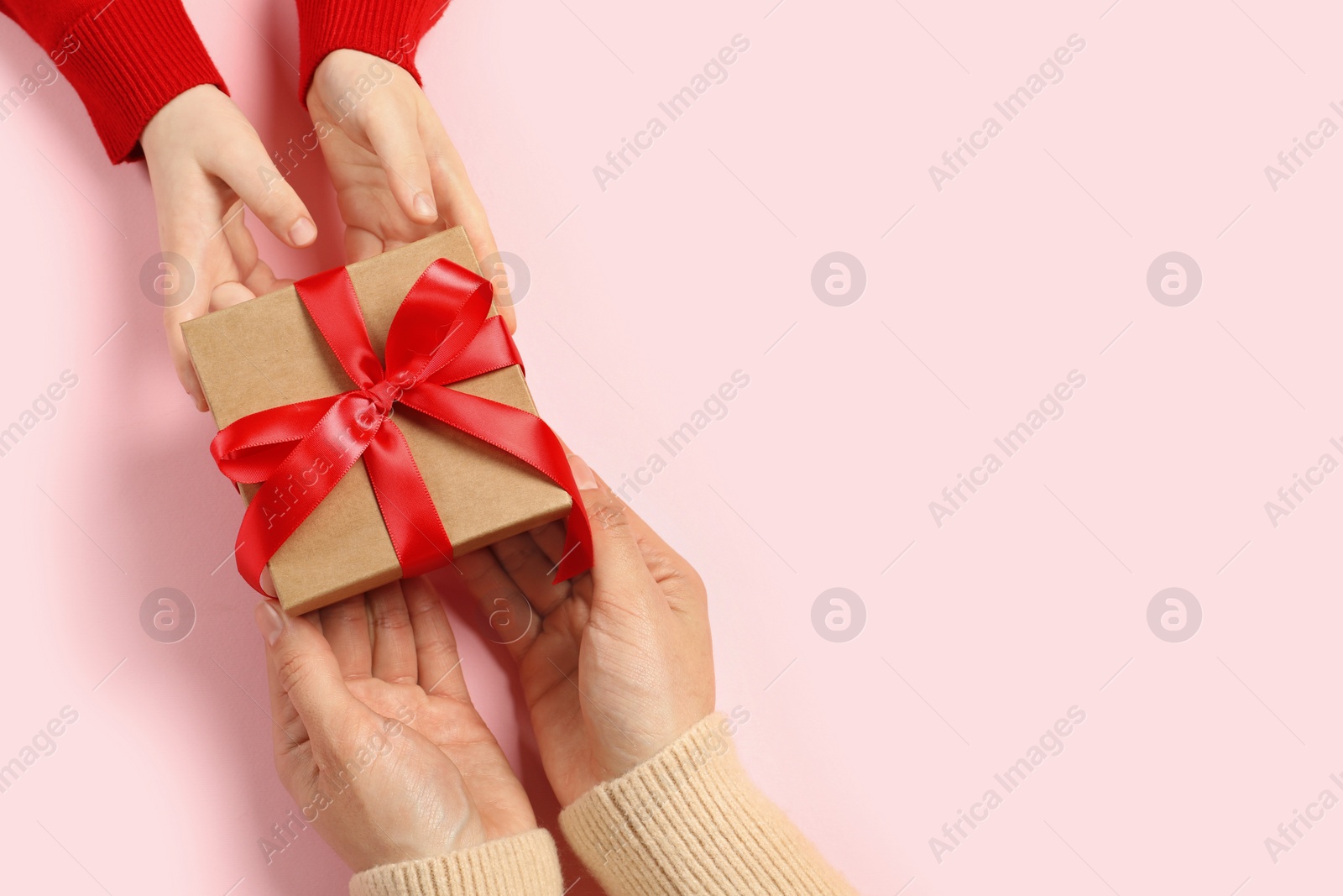 Photo of Mother giving gift box to her child on pink background, top view. Space for text