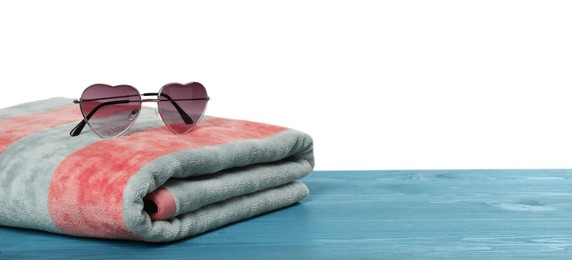 Photo of Beach towel and heart shaped sunglasses on light blue wooden surface against white background. Space for text