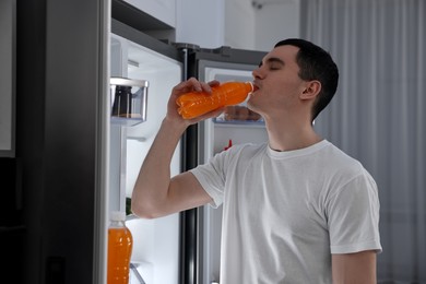 Photo of Man drinking juice near refrigerator in kitchen at night