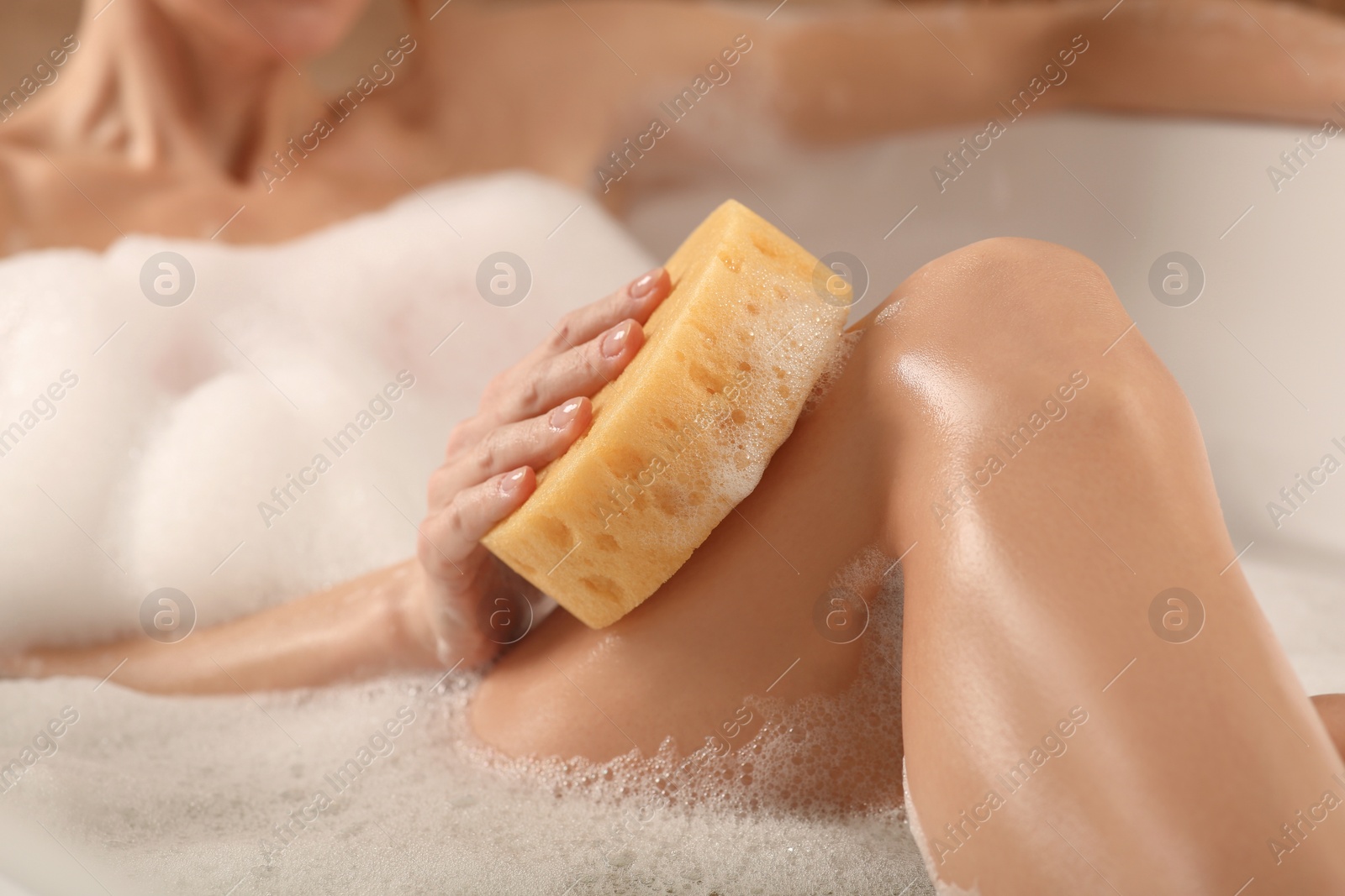 Photo of Woman rubbing her leg with sponge while taking bath, closeup