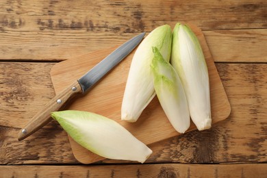 Photo of Fresh raw Belgian endives (chicory), board and knife on wooden table, top view