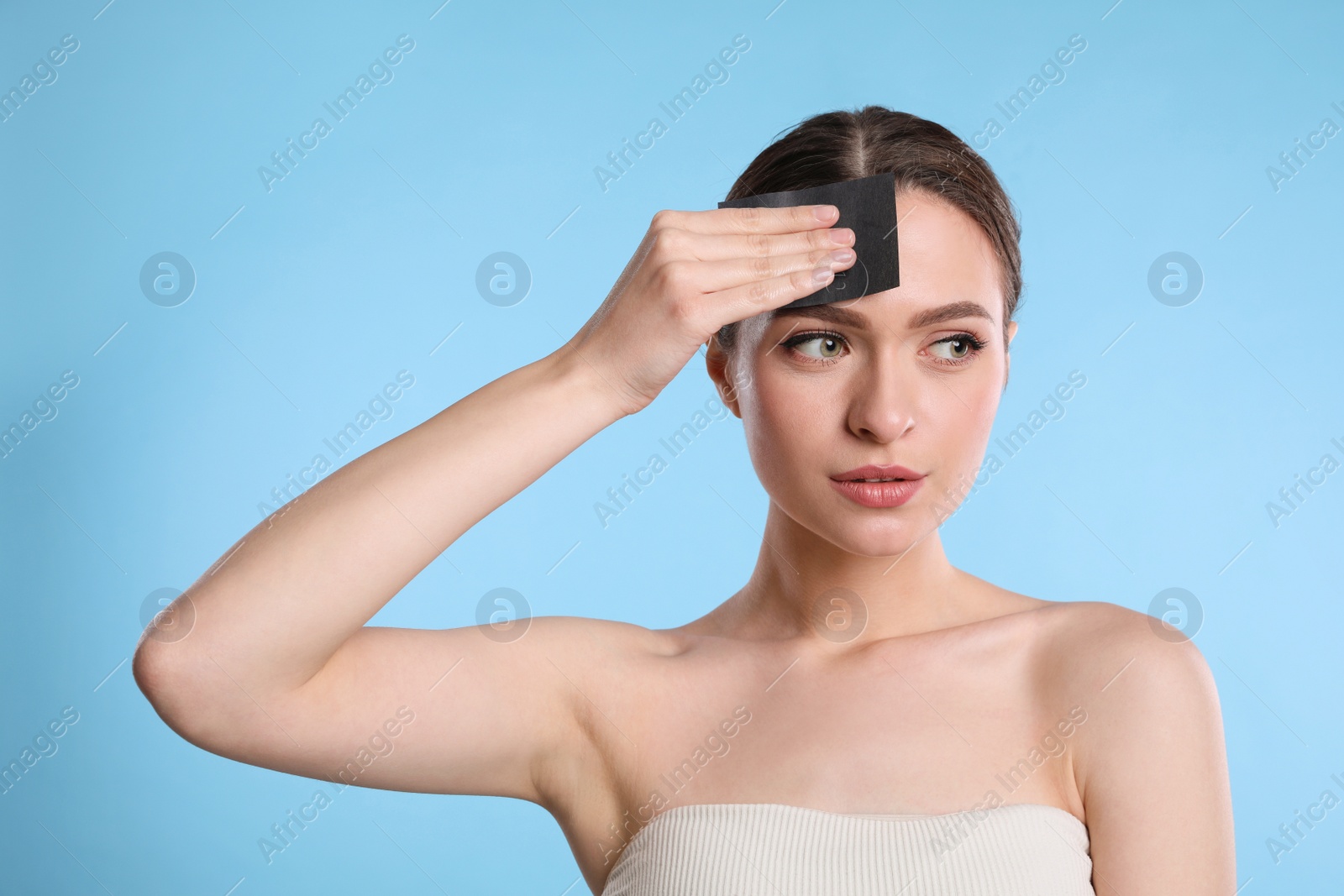 Photo of Beautiful woman using mattifying wipe on light blue background