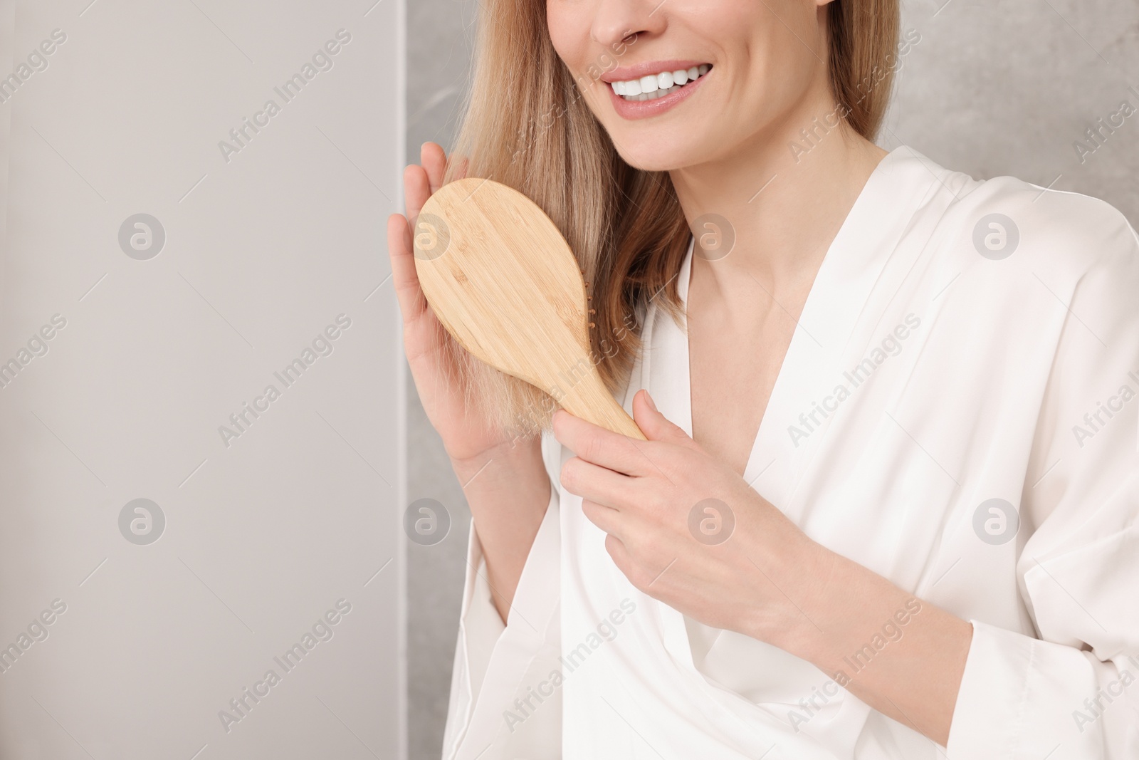 Photo of Woman in white robe brushing her hair indoors, closeup