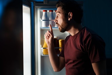 Photo of Man choosing food from refrigerator in kitchen at night. Bad habit